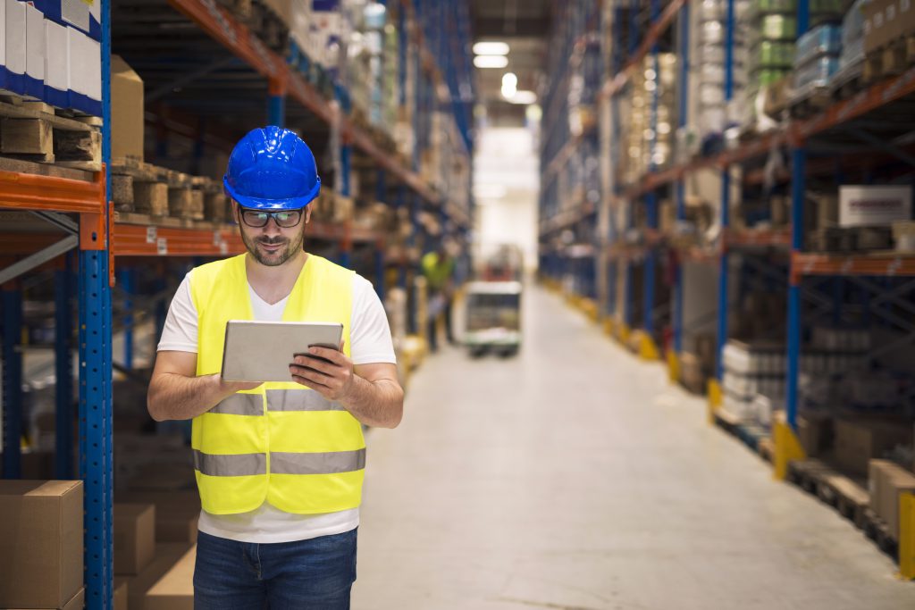 warehouse worker checking inventory his tablet while walking large storage department with shelves packages background scaled 1